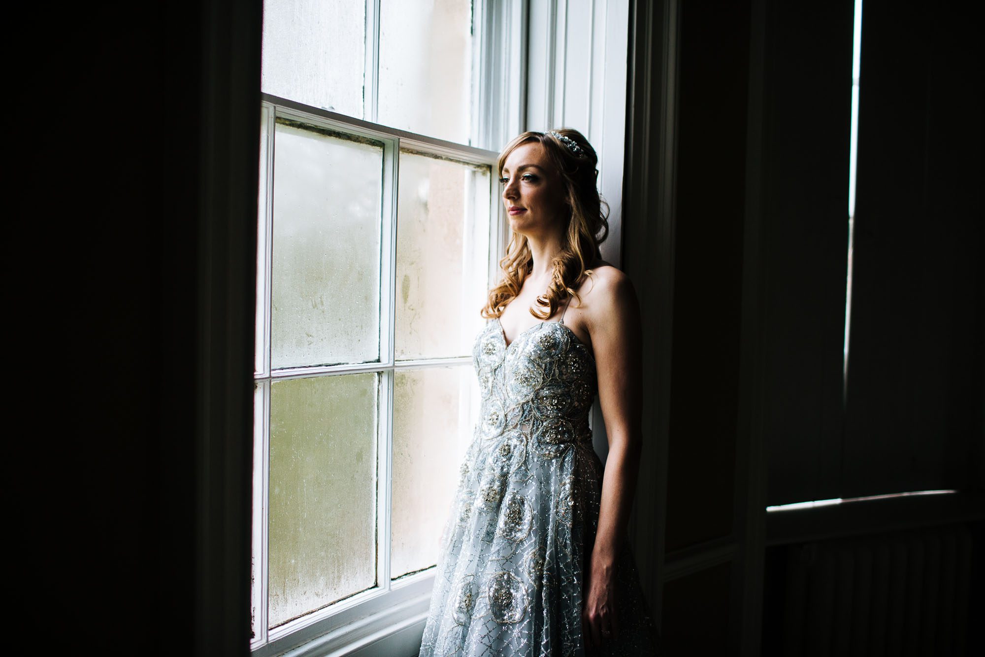 Bride in silver dress standing in the window light