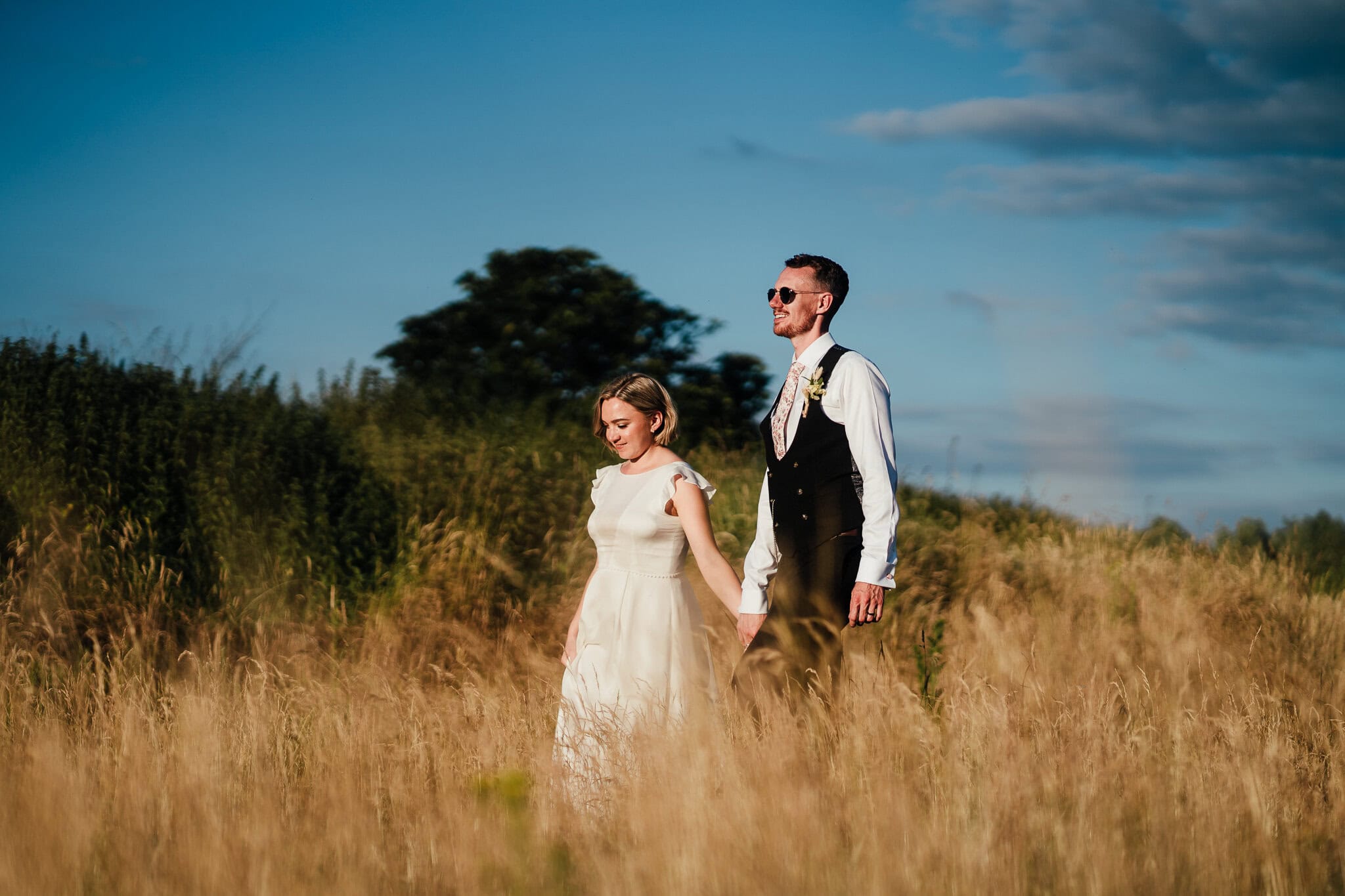 bride and groom waking through long grass hand in hand